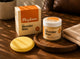 A jar of Payton Wonder Wax and its matching box are displayed on a wooden tray next to a yellow applicator pad on a warm wooden table.
